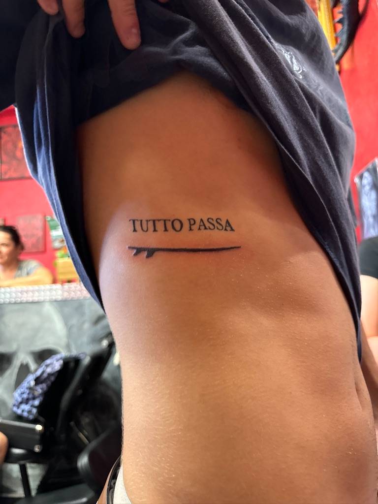 Tutto Passa tattoo with a surfboard line underneath