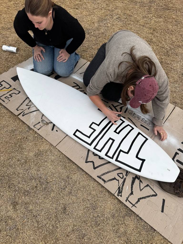 Inking THE onto the surfboard in outlined block letters